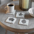 Coasters with leaf design on a round wooden table with a cup of coffee.