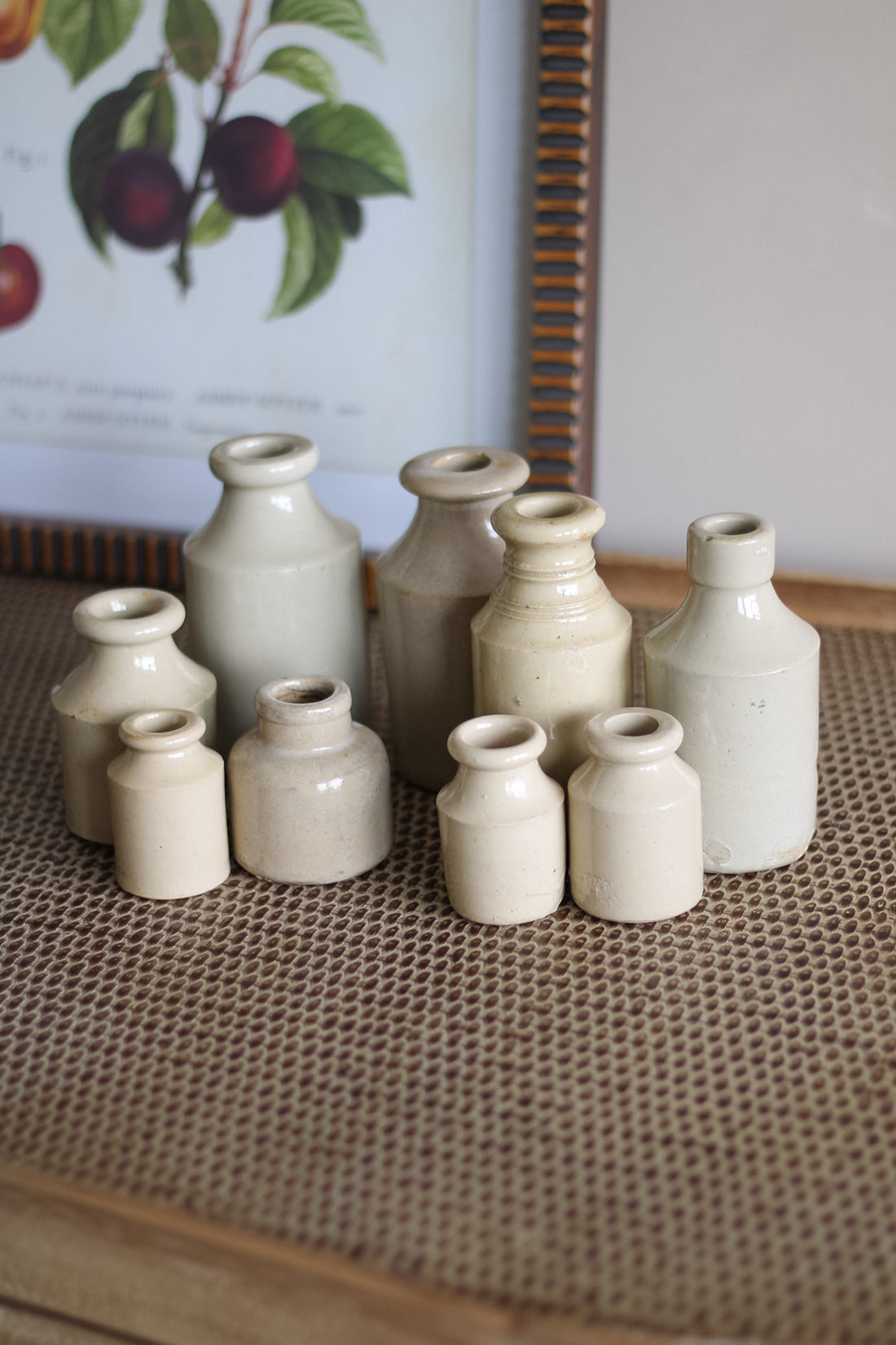 Collection of ceramic bottles on a textured surface with a framed picture in the background.