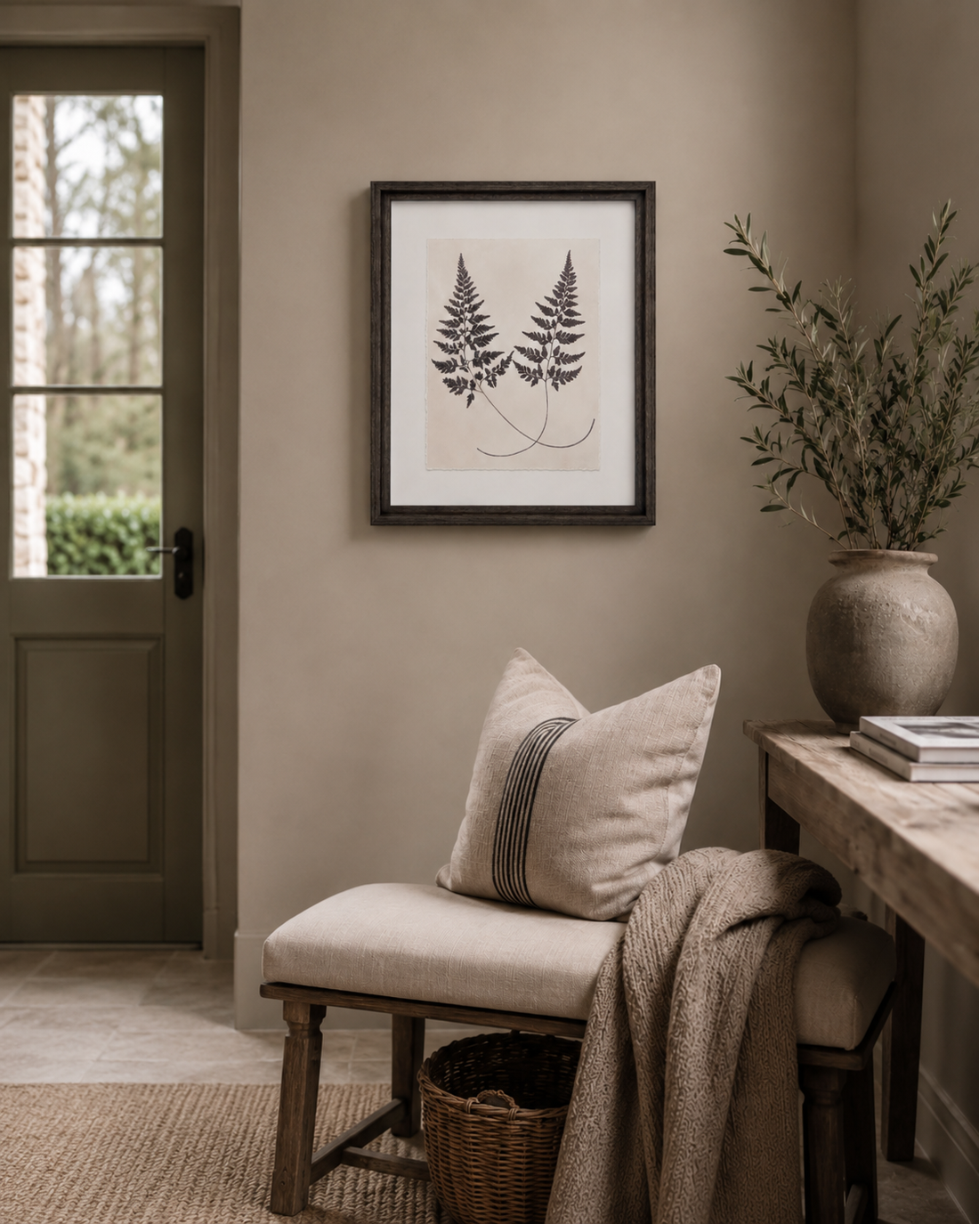 Nestled corner of a room with a bench, pillows, a vase, and framed fern vintage style artwork on a beige wall.