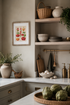 A framed botanical art print featuring colorful tomatoes and peppers hangs on a beige wall in a styled kitchen setting with wooden shelves, white dishes, and a marble countertop.