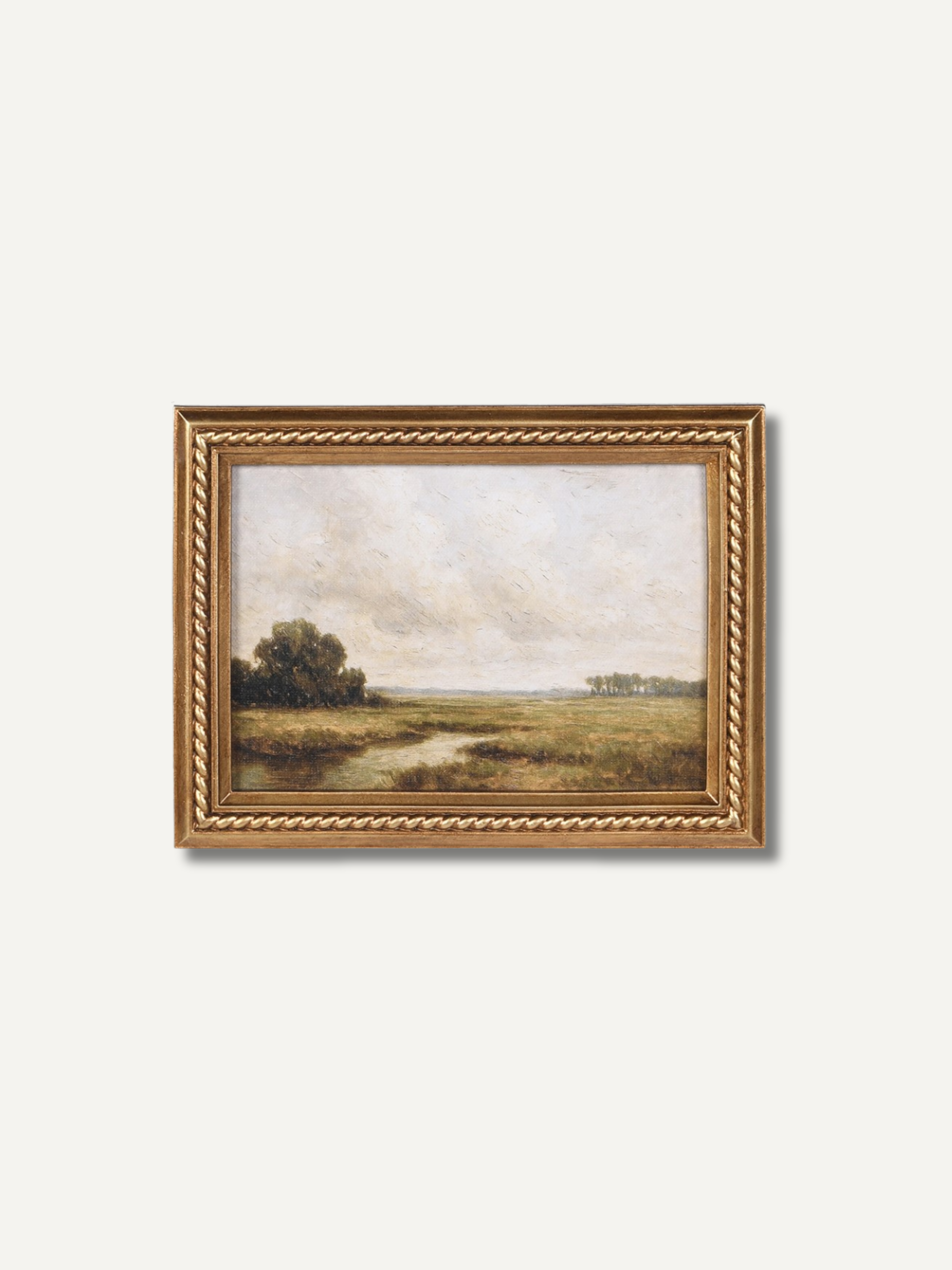 A framed landscape painting featuring a grassy field, a winding path, and a tree on the left, enclosed in an ornate gold frame against a light gray background.