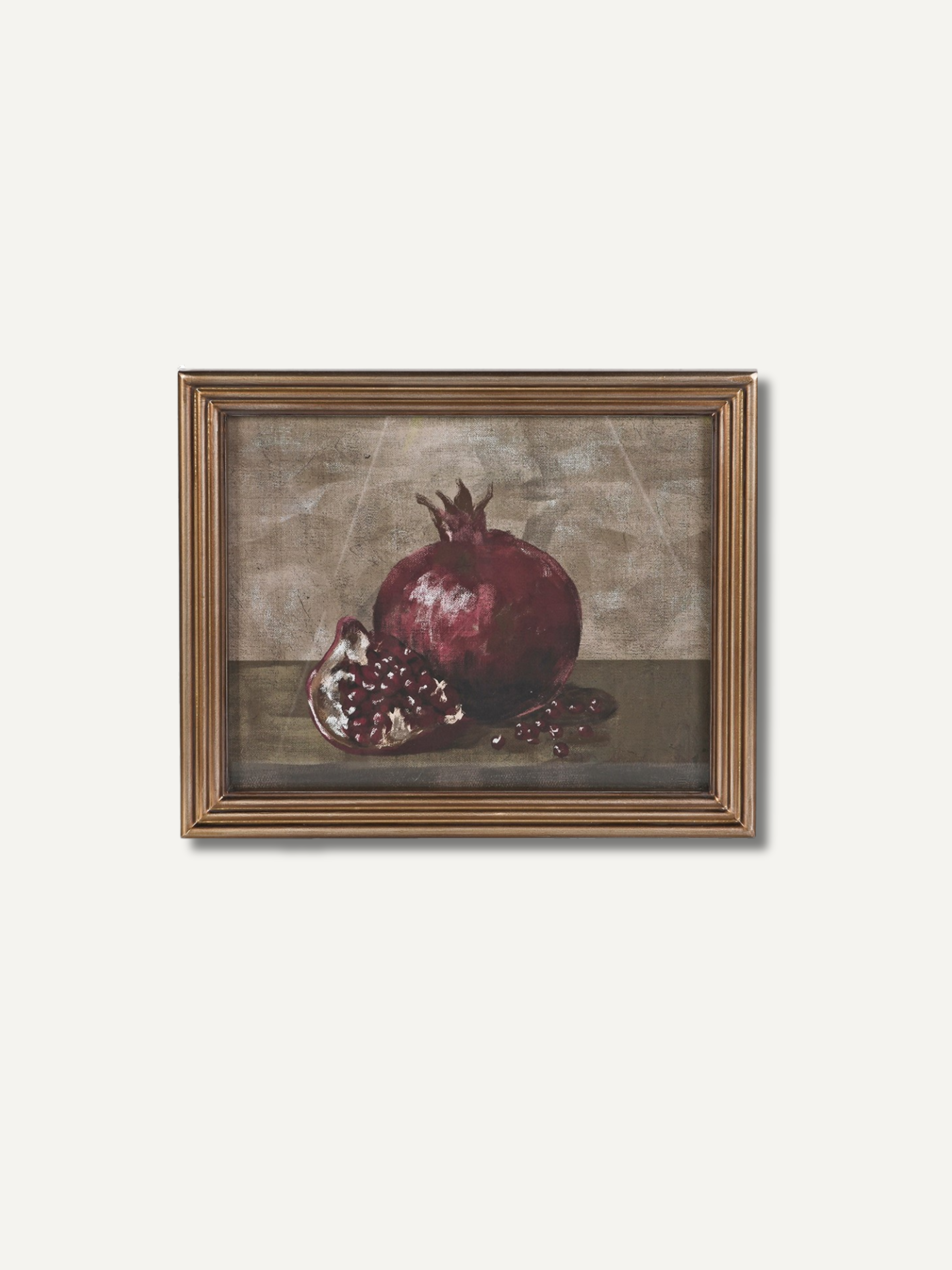 A framed still life painting of a pomegranate, featuring a whole and halved pomegranate on a dark surface against a textured beige-brown background, enclosed in a gold-toned frame.