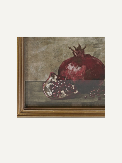 A framed still life painting depicting a whole and halved pomegranate on a muted textured background, shown against a light off-white backdrop.
