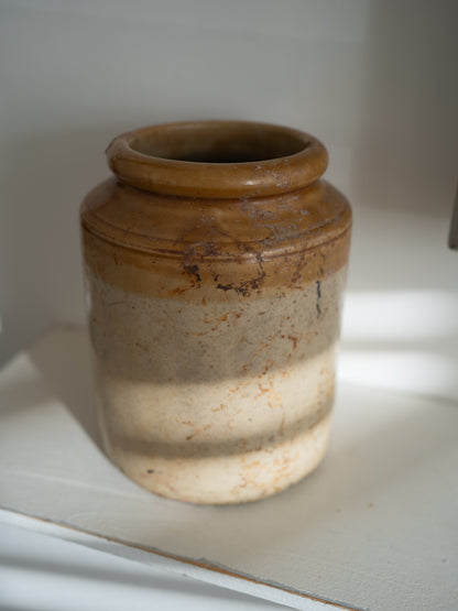A vintage ceramic vintage storage jar with a two-tone glaze, featuring a warm brown top section and a textured cream-beige bottom section, displayed on a white shelf.