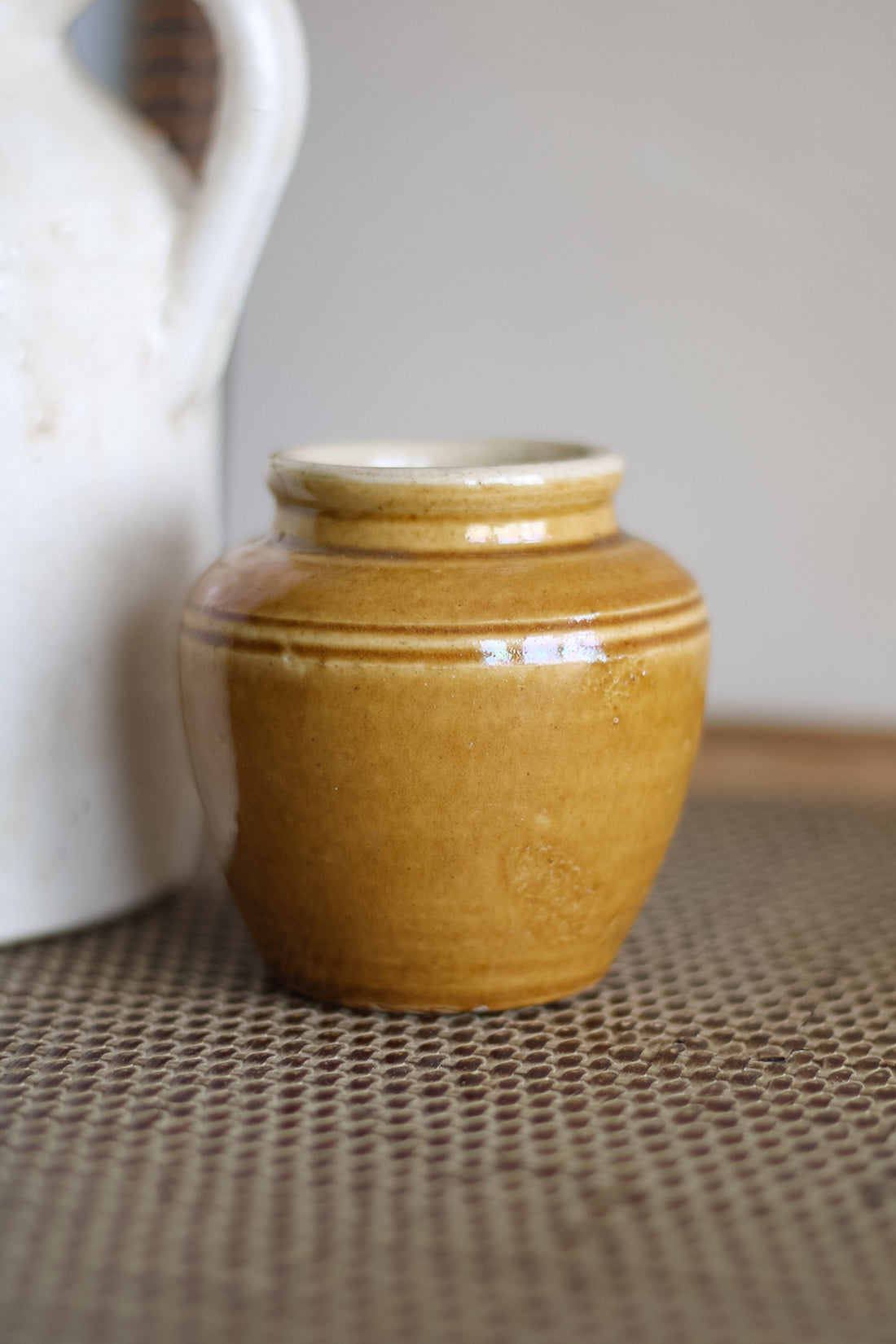 Yellow ceramic jar on a textured surface with a blurred white object in the background