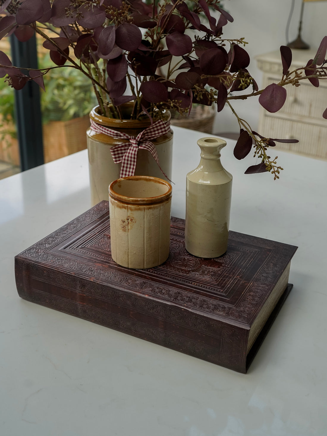 Decorative arrangement with ceramic jars and a book on a white surface