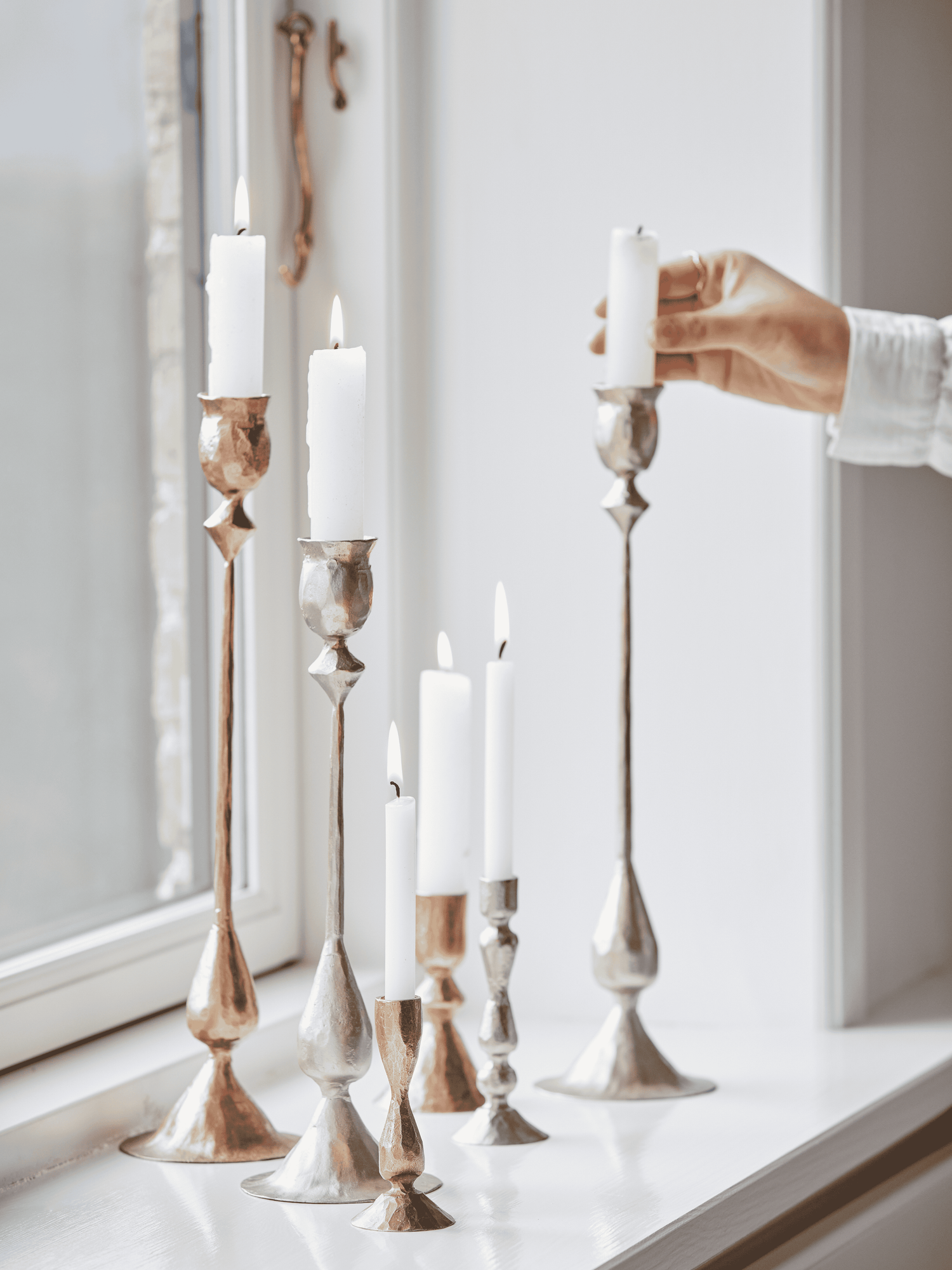 Decorative mixed metal silver and gold vintage inspired candlesticks with candles on a windowsill, timeless home decor and styling ideas