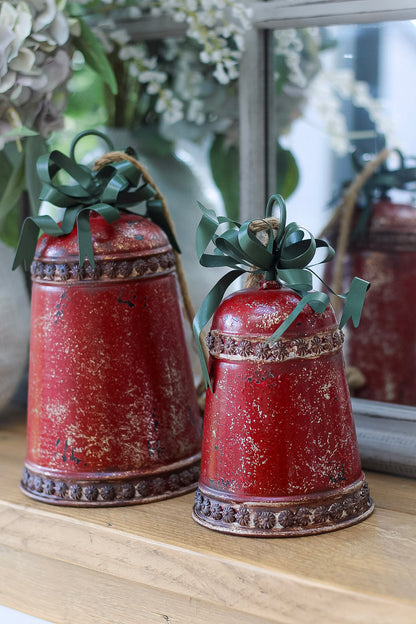 Two red decorative bells with green ribbons on a wooden surface.