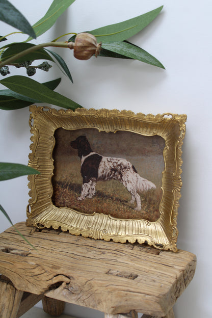 Decorative framed picture of a dog on a wooden surface with green leaves in the background