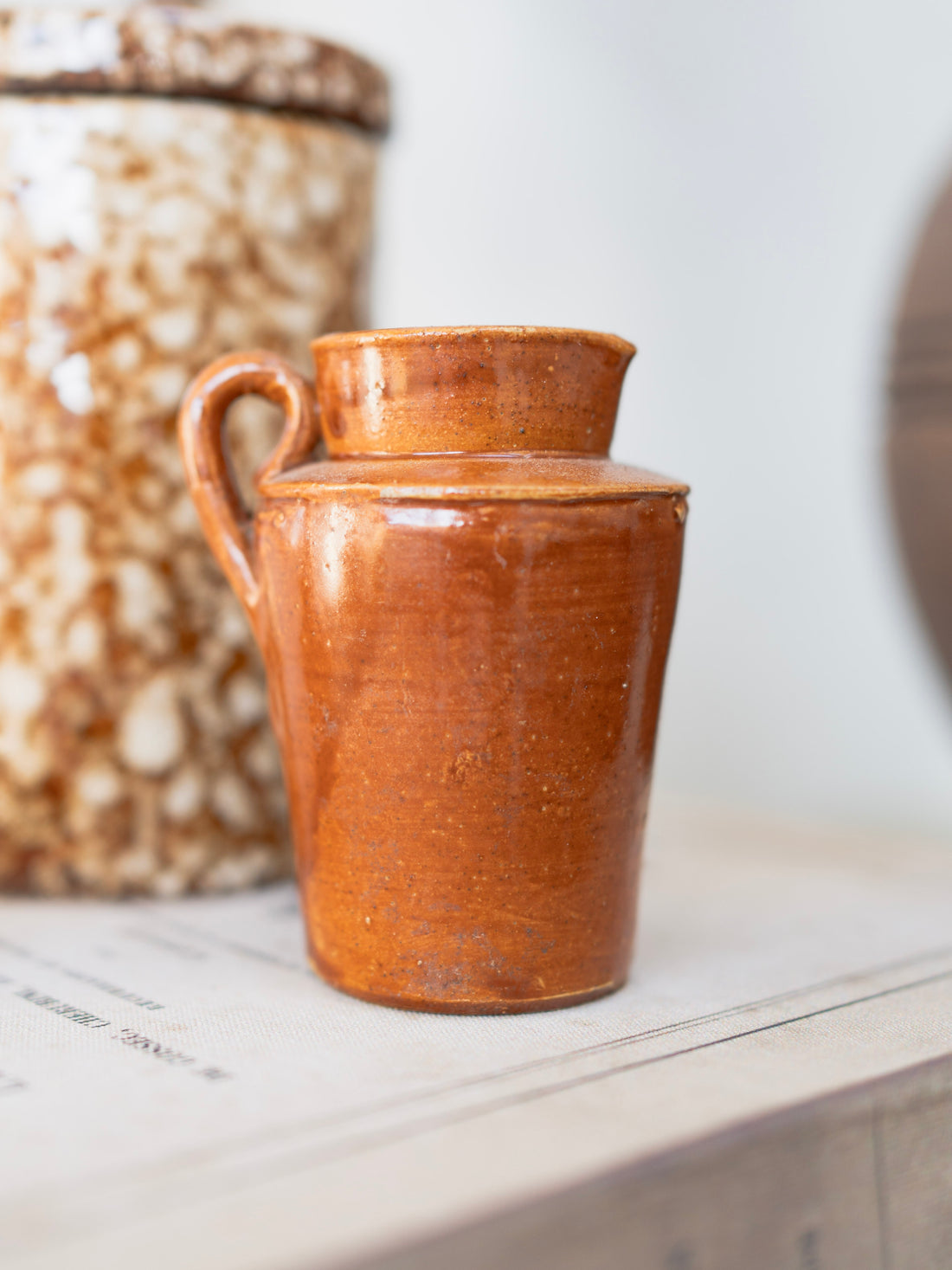 Vintage brown ceramic small jug on a white surface with a blurred background