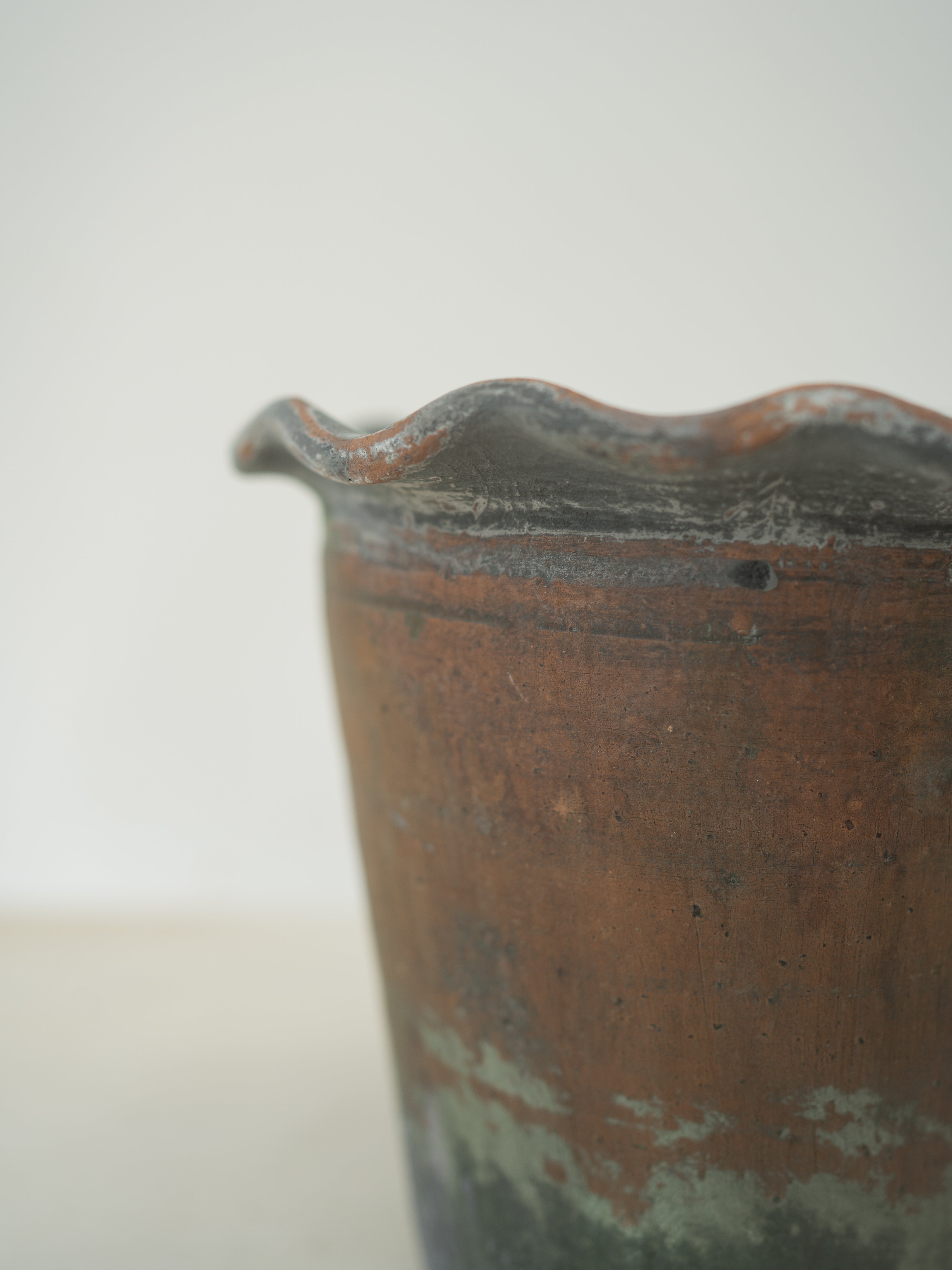 Rust-colored ceramic vase with wavy rim on a light gray background