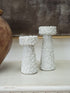 Two white textured decorative candle holders with a bubbly, coral-like surface finish, displayed on a light surface next to a wooden vase against a neutral background.