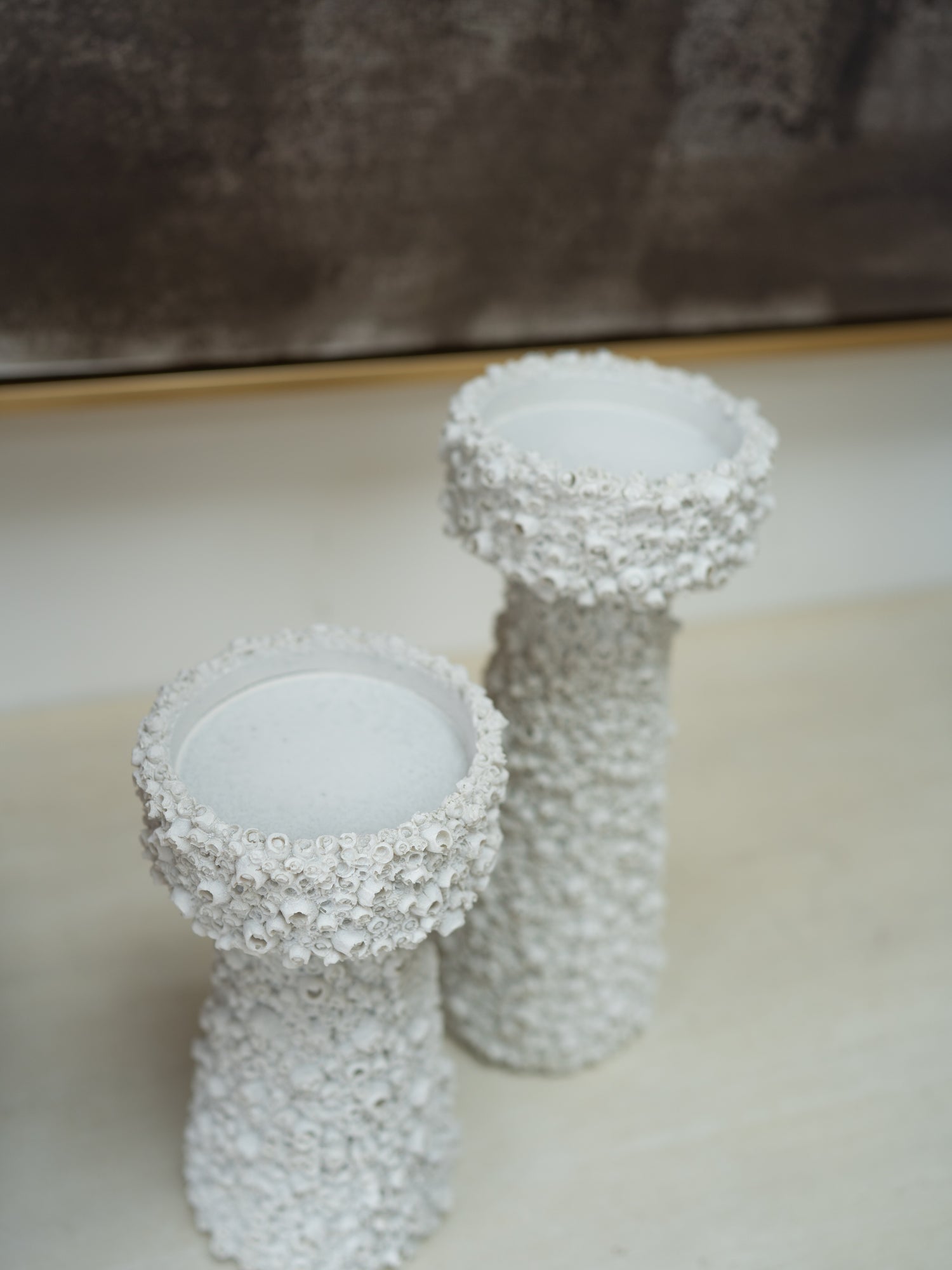 Two white textured pillar candle holders with a bubbly, coral-like surface finish, displayed on a light beige surface against a neutral background.