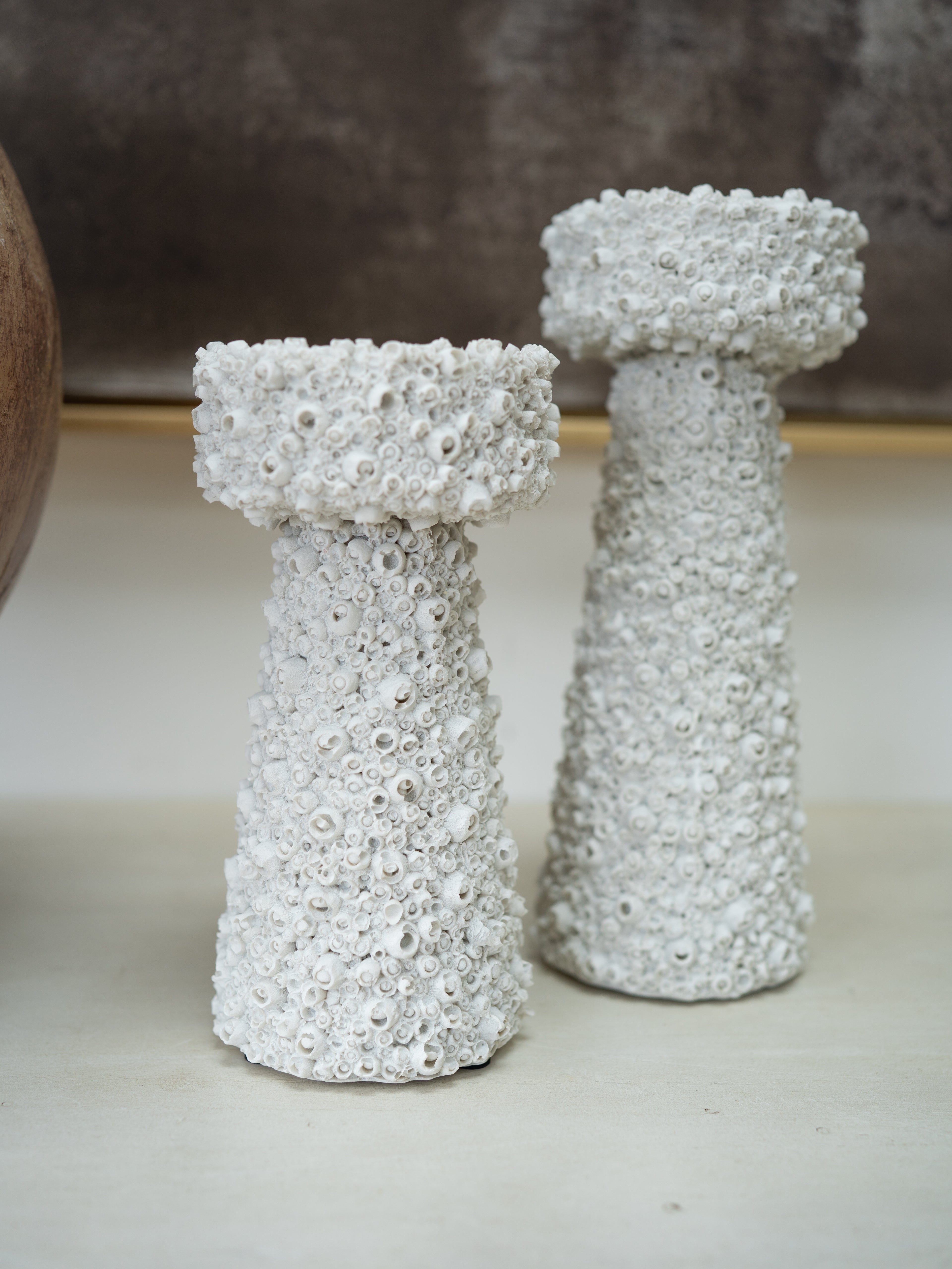 Two white textured decorative candle holders with a bubbly, coral-like surface, standing on a light surface against a neutral background.