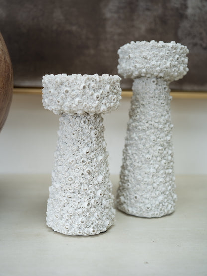 Two white textured decorative candle holders with a bubbly, coral-like surface, standing on a light surface against a neutral background.