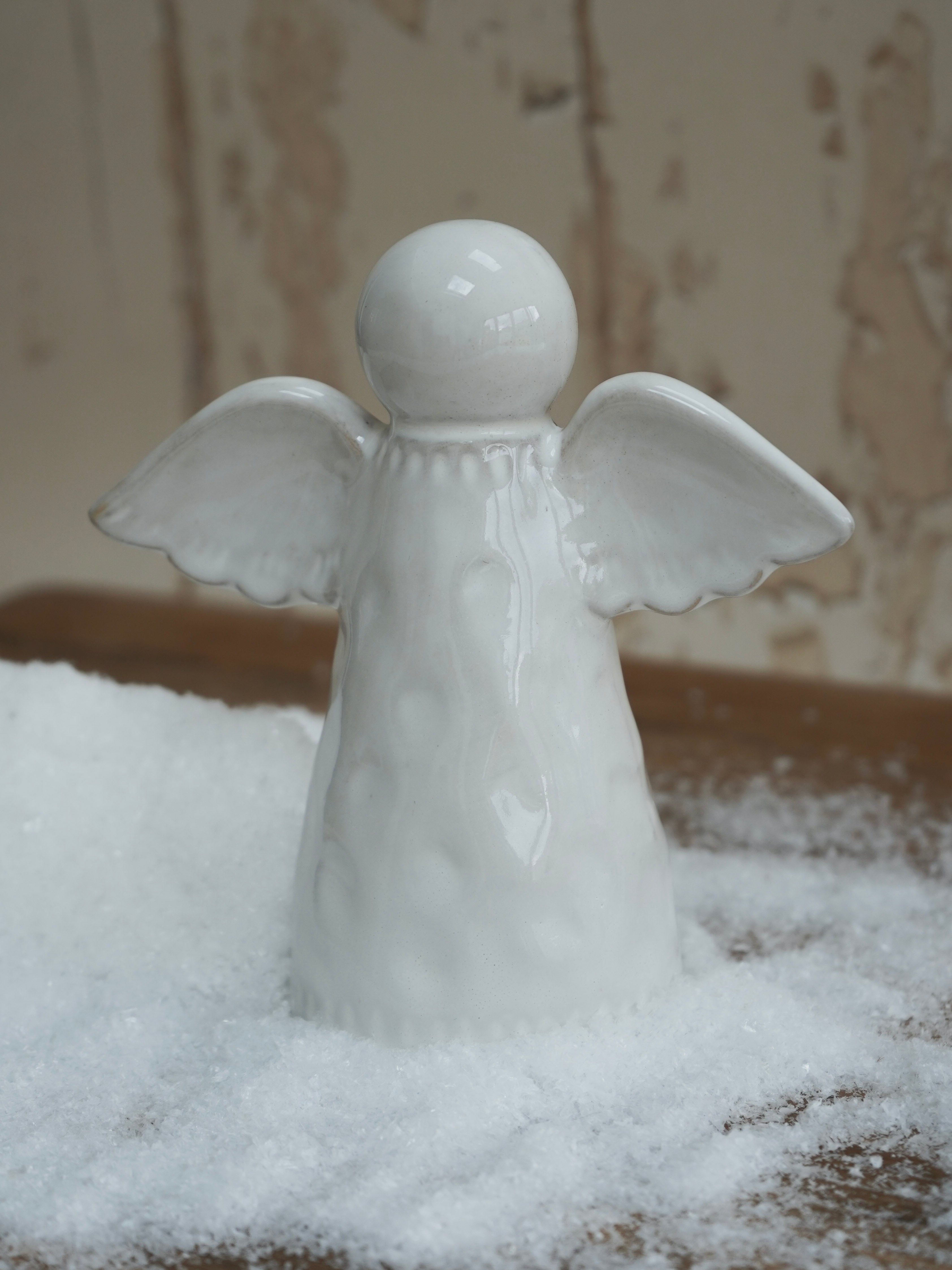 White ceramic angel figurine on a snowy surface with a neutral background