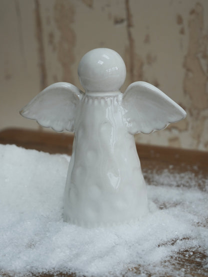 White ceramic angel figurine on a snowy surface with a neutral background
