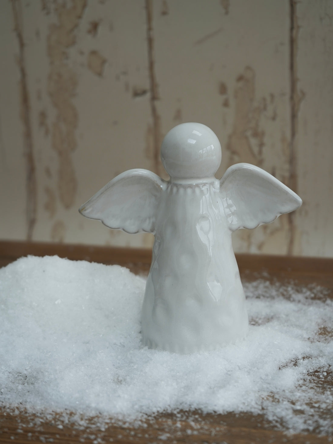 White angel figurine on a bed of artificial snow with a neutral background