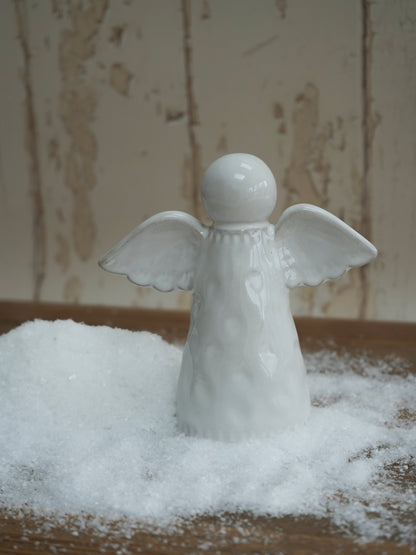 White angel figurine on a bed of artificial snow with a neutral background