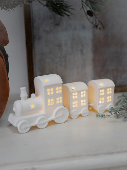 White ceramic train decoration with lit-up windows on a white surface.