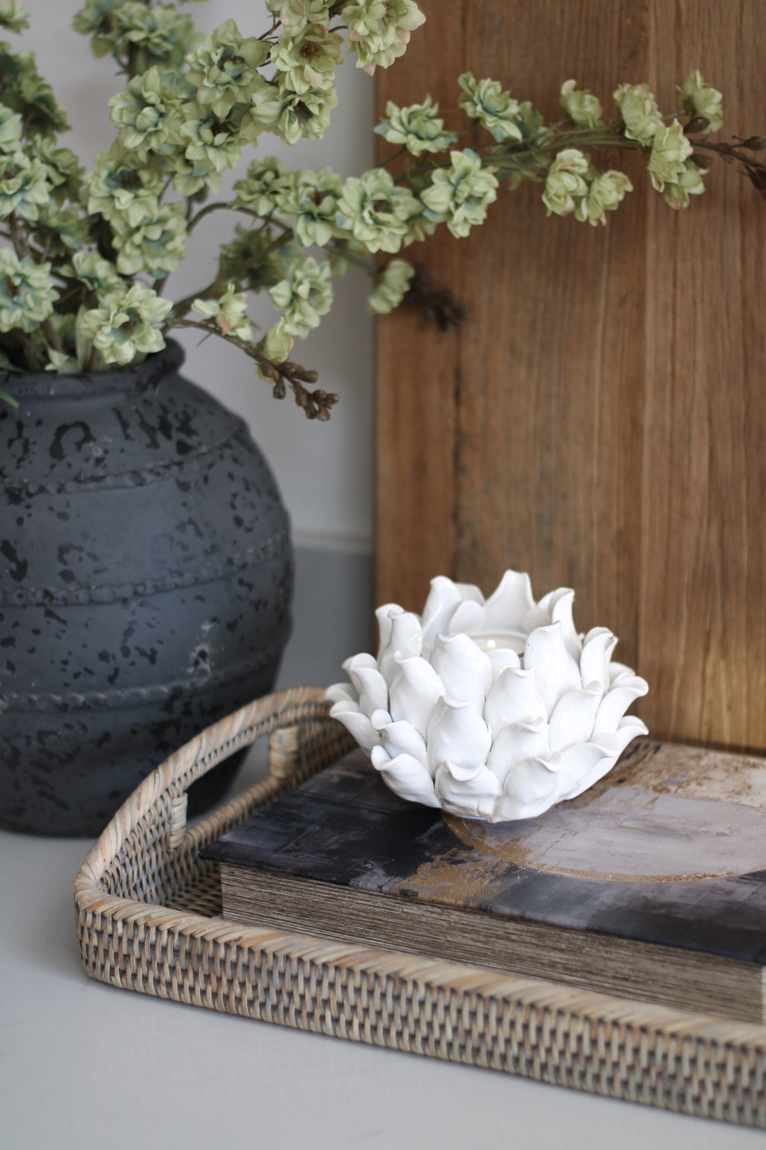 Decorative setting with a textured candle, white ceramic flower, and wicker