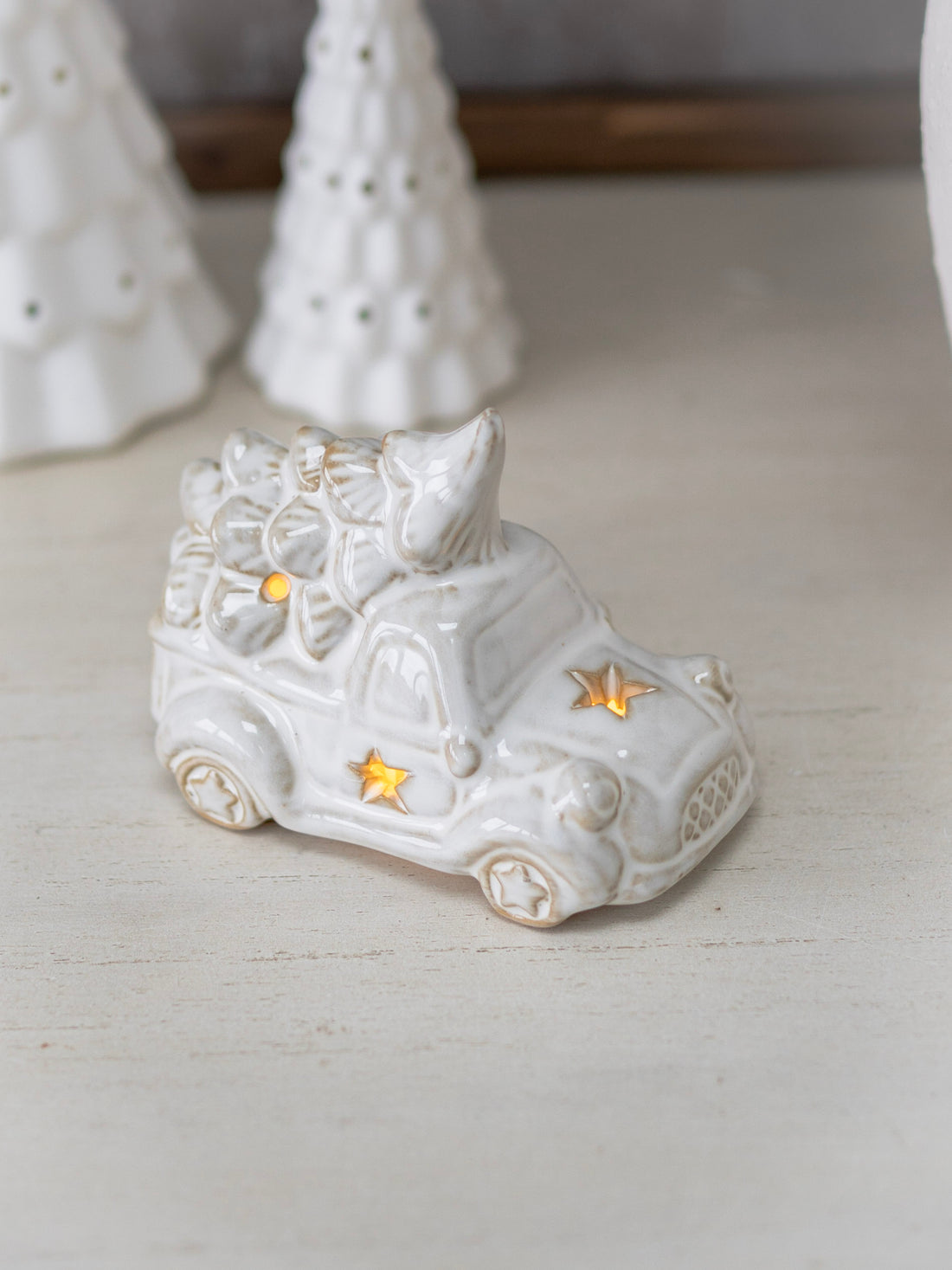 White ceramic car ornament with decorative elements on a light wooden surface.