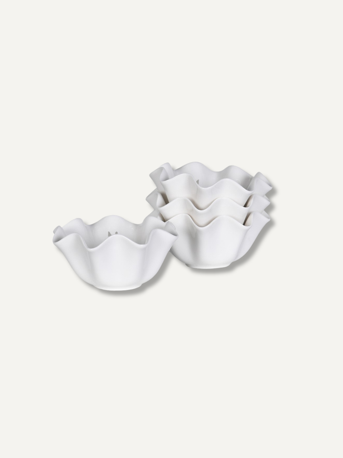Four white ceramic ruffled bowls, with three stacked and one standing, on a light beige background.