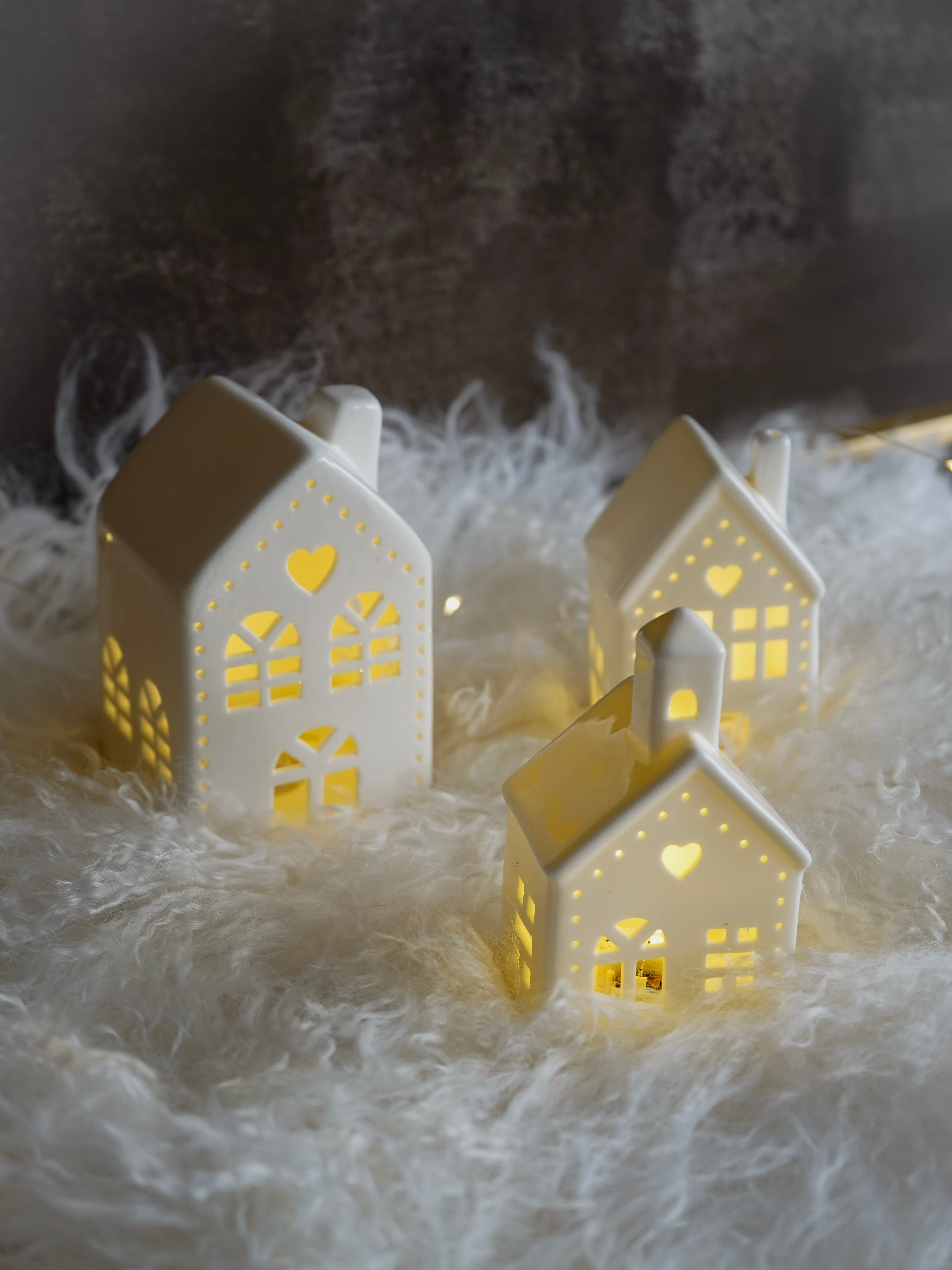 Two white ceramic house-shaped lanterns with cut-out windows on a soft, textured surface.