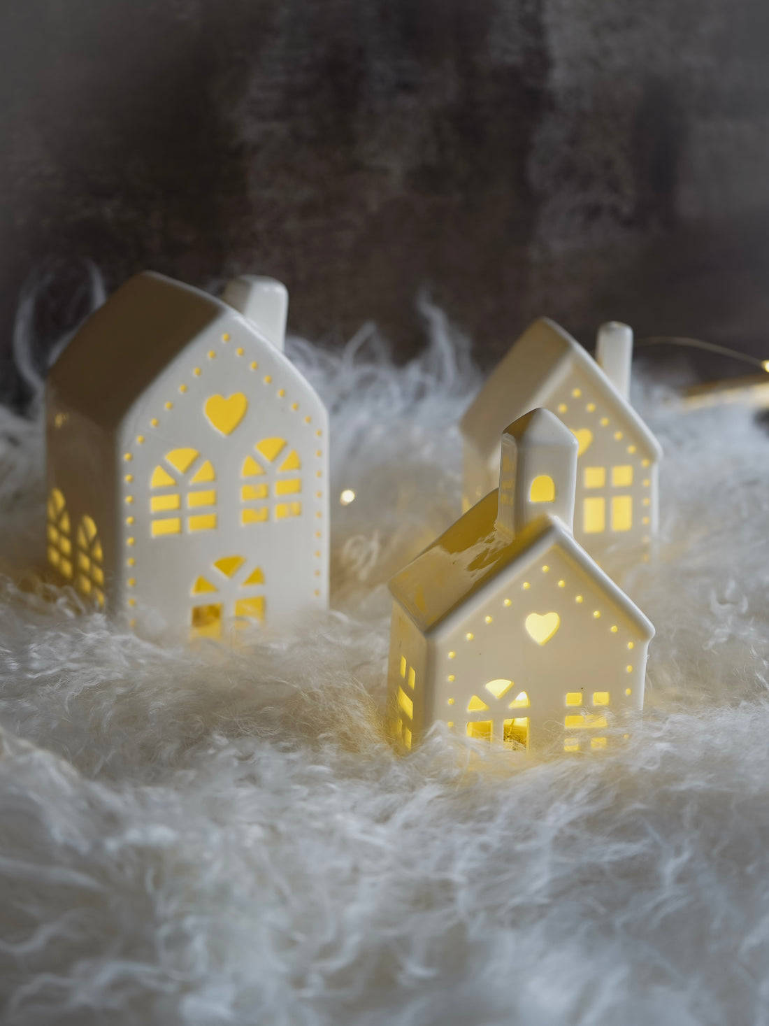 Two illuminated white house-shaped lanterns on a soft, white surface with a dark background.
