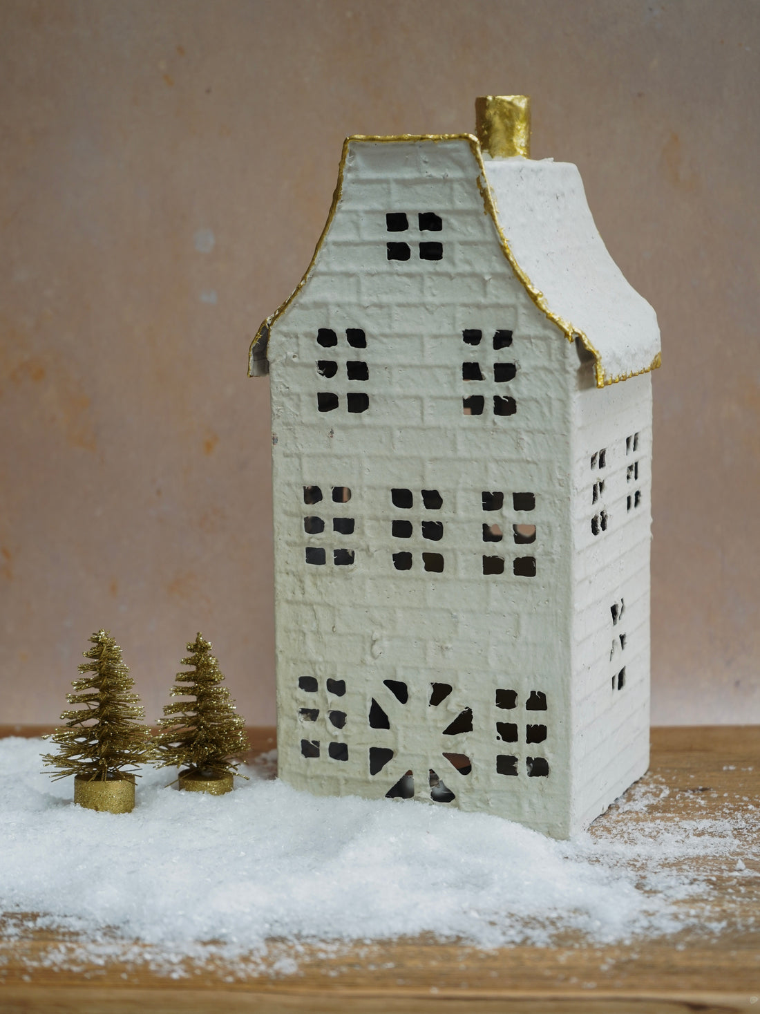 Model of a house with a snowy base and small trees on a wooden surface