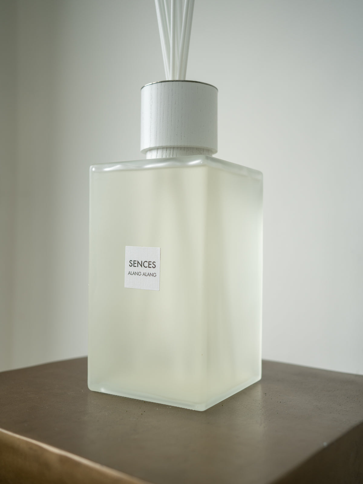 A frosted glass reed diffuser bottle with a white cap and white reeds, labeled &