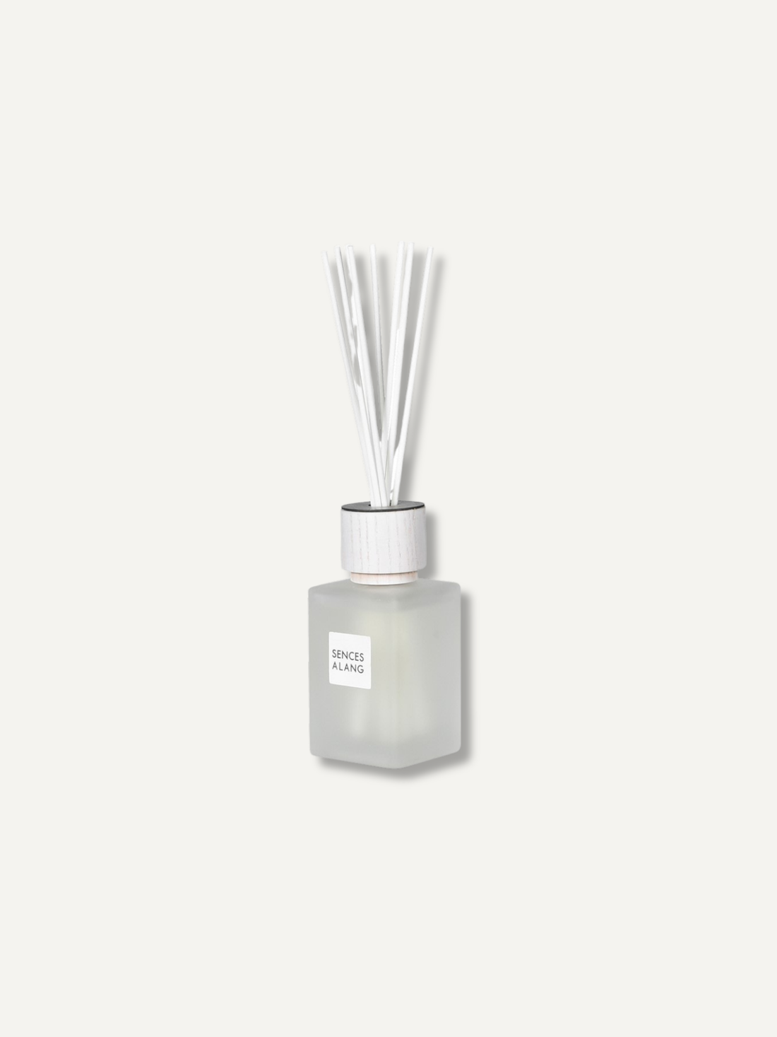 A frosted glass reed diffuser bottle with a white cap and clear reeds, centered on a light off-white background. The label reads &