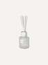A frosted glass reed diffuser bottle with a white cap and clear reeds, centered on a light off-white background. The label reads &