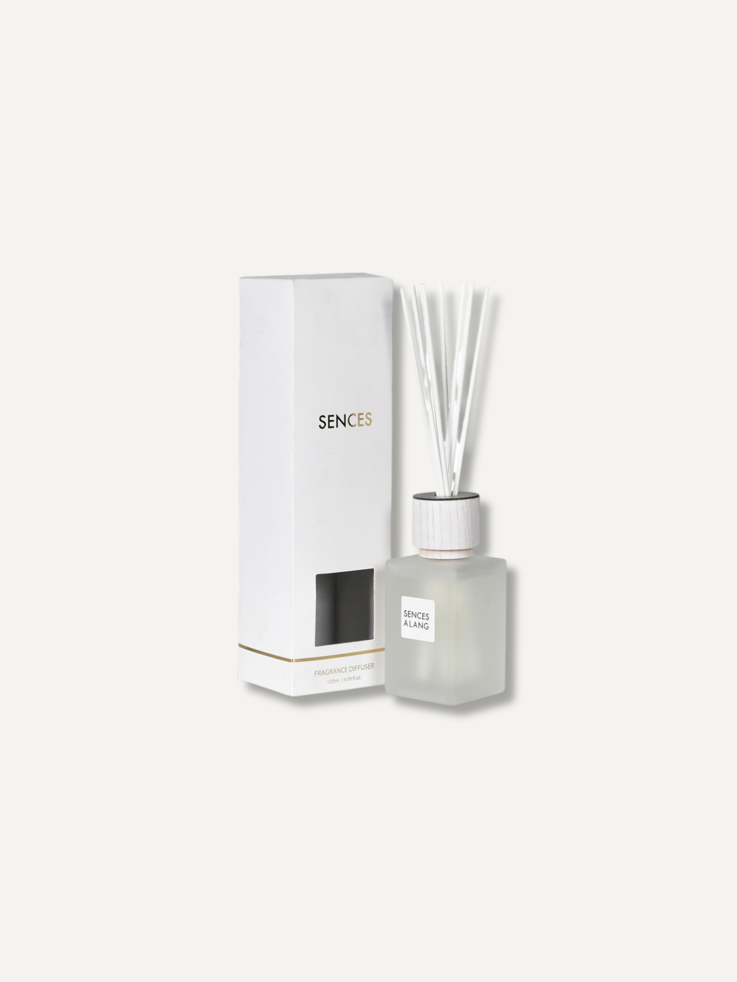 A reed diffuser bottle with translucent glass, white reeds, and a white cap, shown next to its tall white box on a light warm gray background. The box is labeled &
