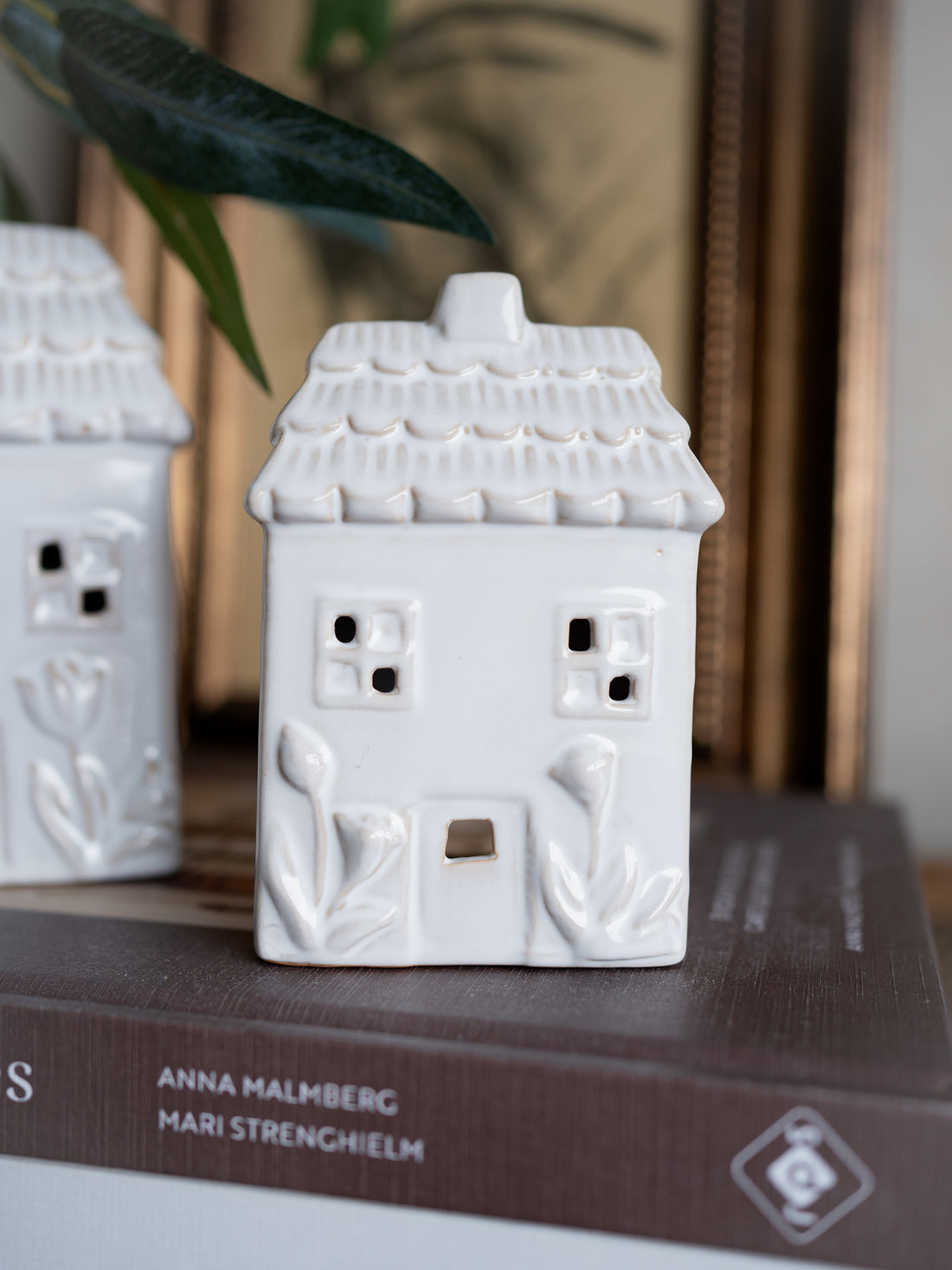 White ceramic house-shaped lantern on a book with a blurred background