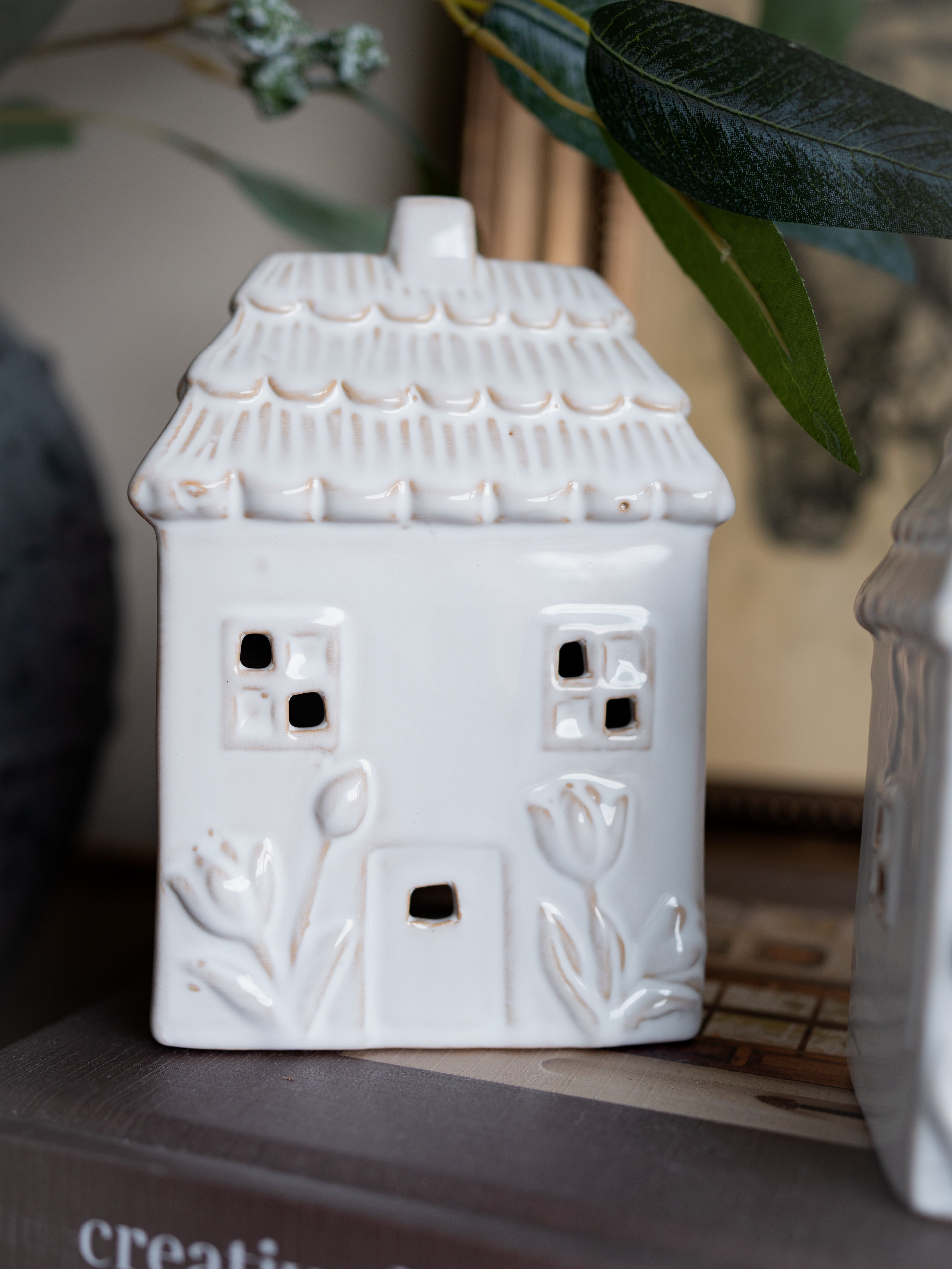 White ceramic house-shaped vase with decorative elements on a surface.