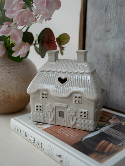 Ceramic house-shaped lantern on a book with pink flowers in the background