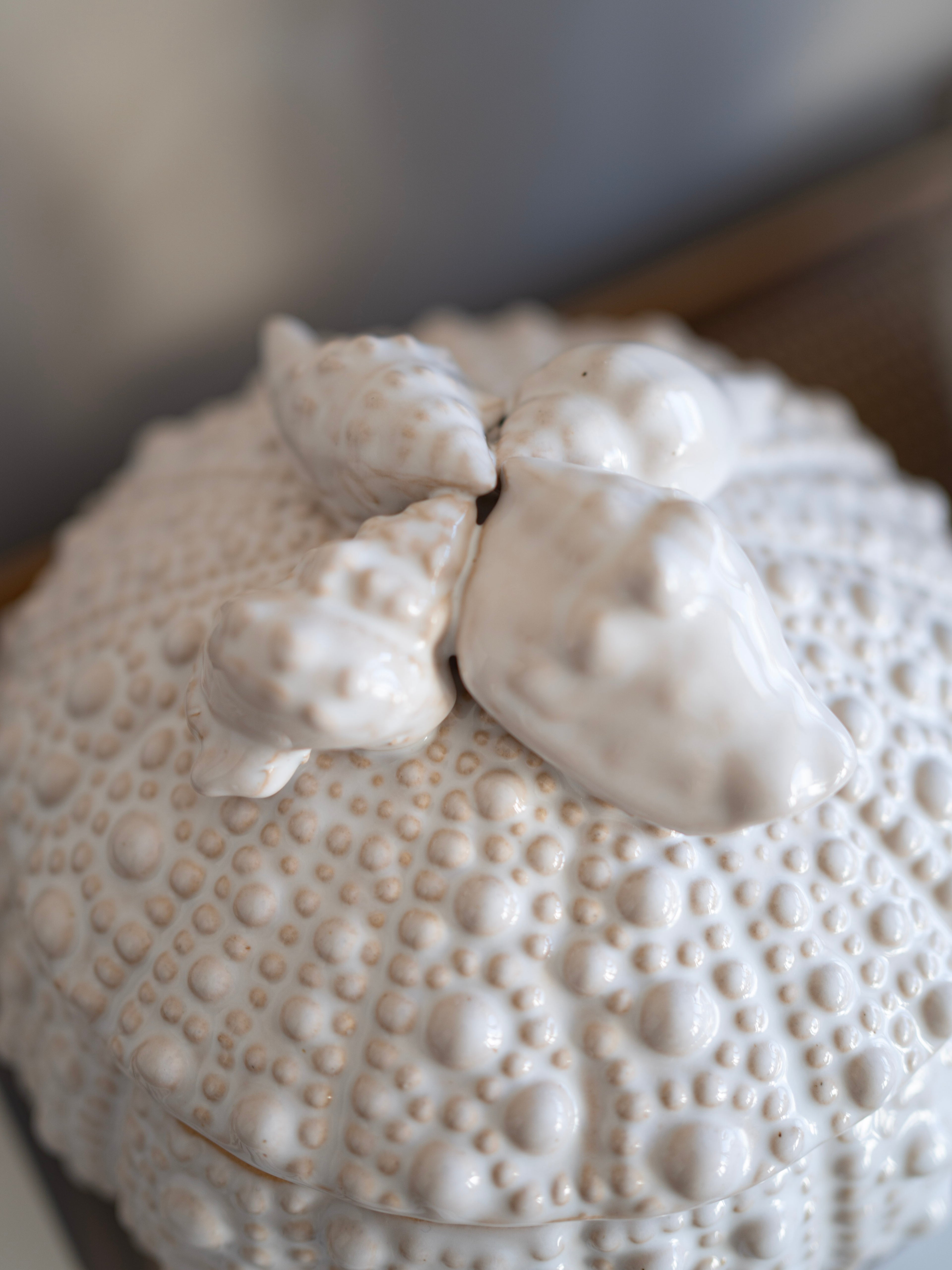 Decorative white ceramic sea urchin jar with textured surface and animal figures on a blurred background