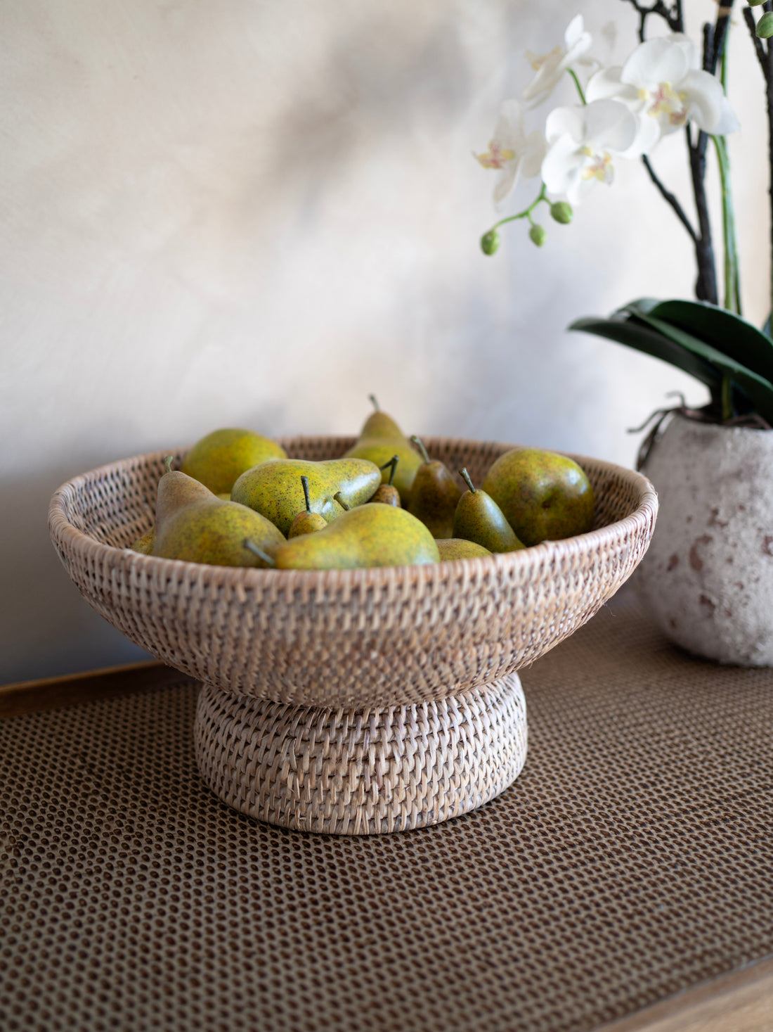 Woven white washed rattan bowl with pears on a textured surface with a blurred background