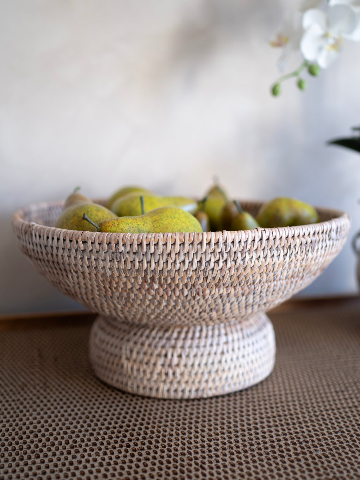 Woven pedestal fruit bowl with fruits on a textured surface