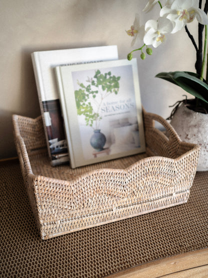 white washed woven rattan basket tray with books and a plant on a textured surface