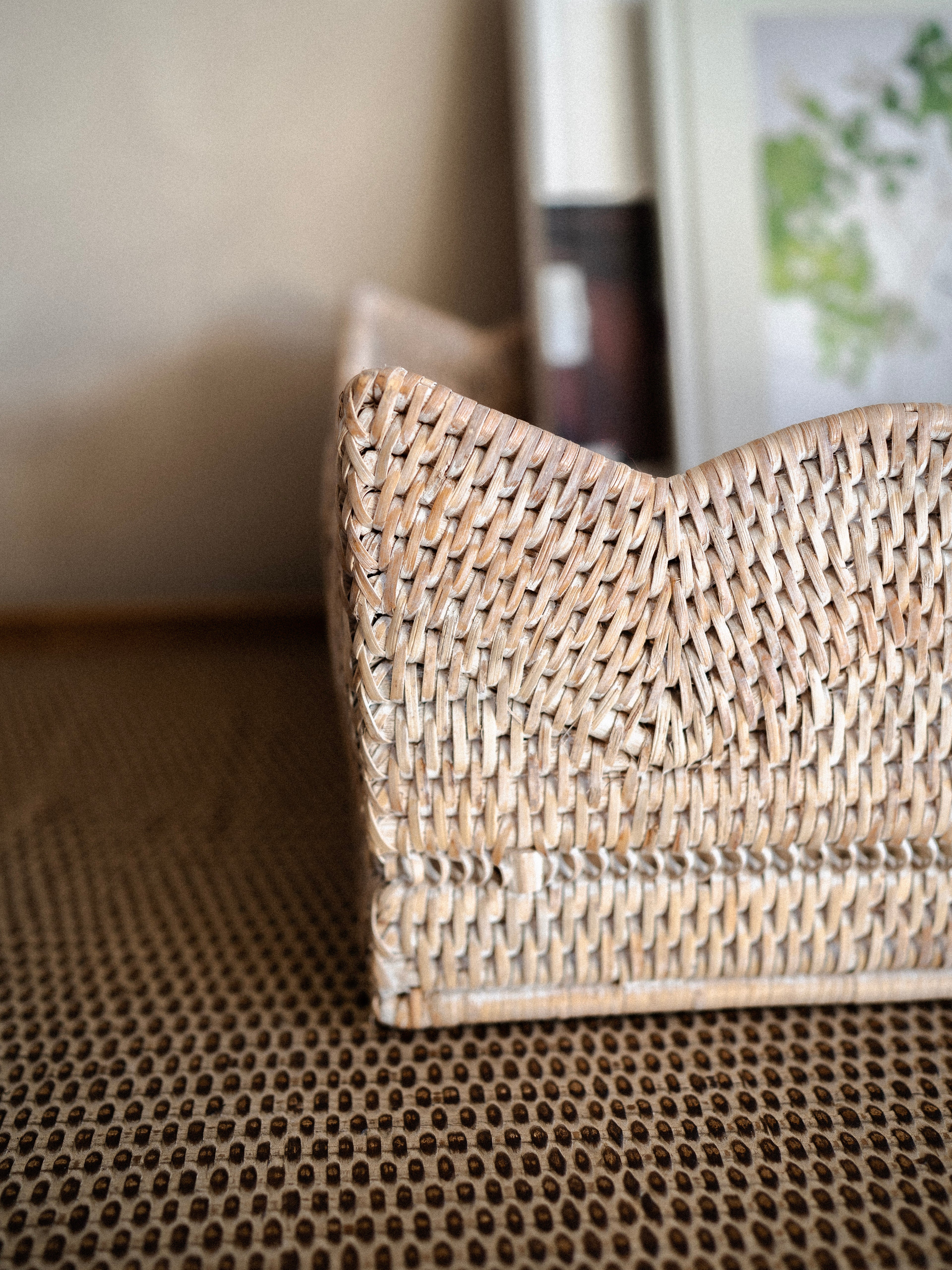 White washed woven rattan rectangular basket tray on a textured surface with a blurred background