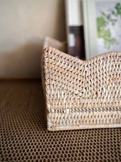 White washed woven rattan rectangular basket tray on a textured surface with a blurred background