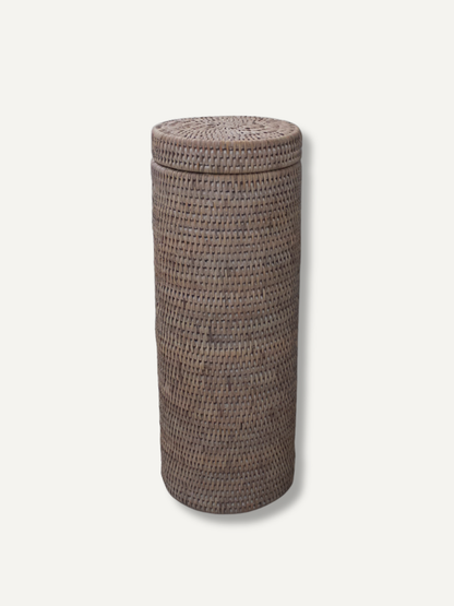 A tall, cylindrical white  white washed rattan toilet roll holder basket with a fitted lid, shown on a plain light background