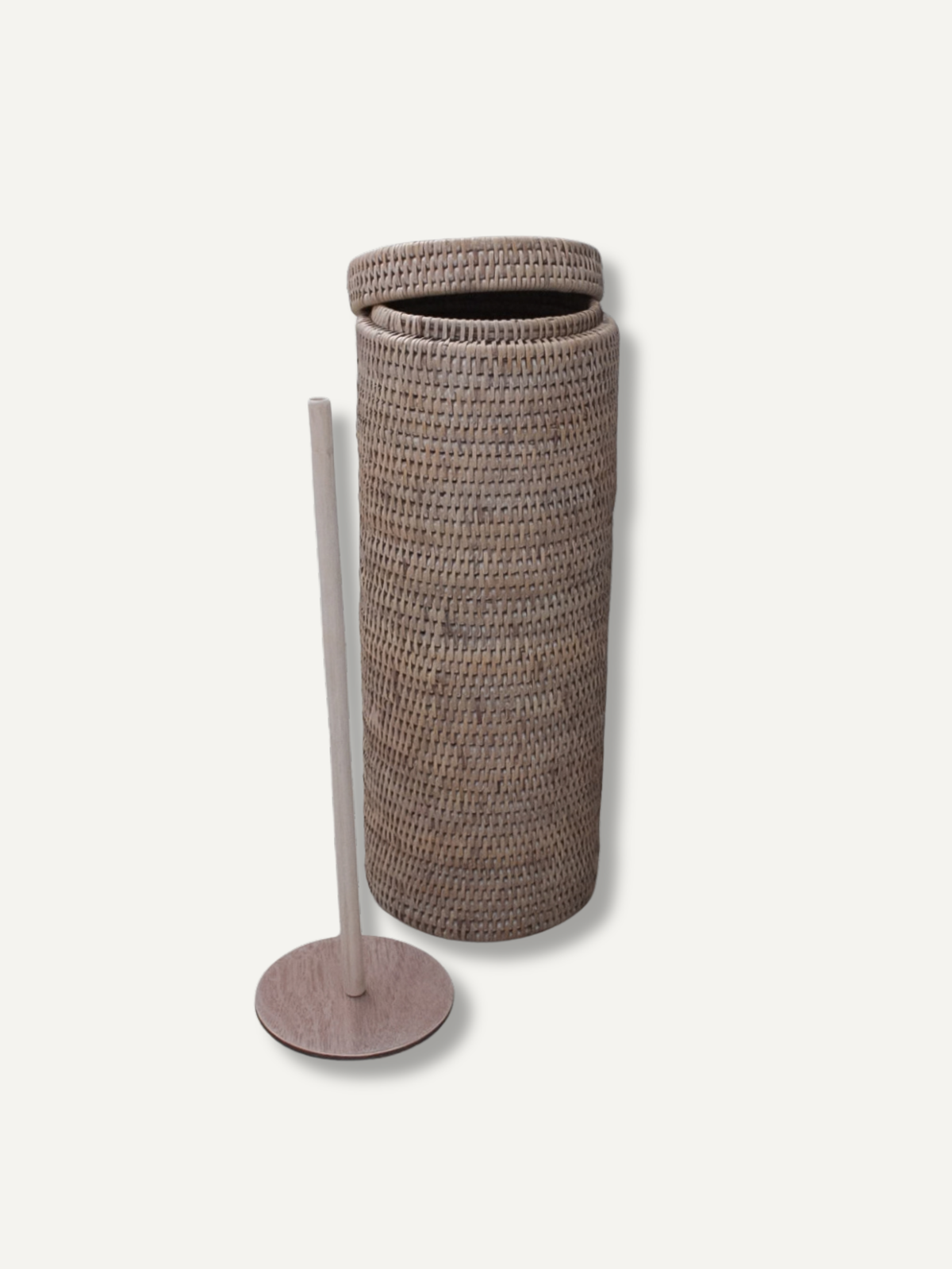 A tall cylindrical woven basket with a matching lid, shown next to a slim light wood floor stand on a plain off-white background.