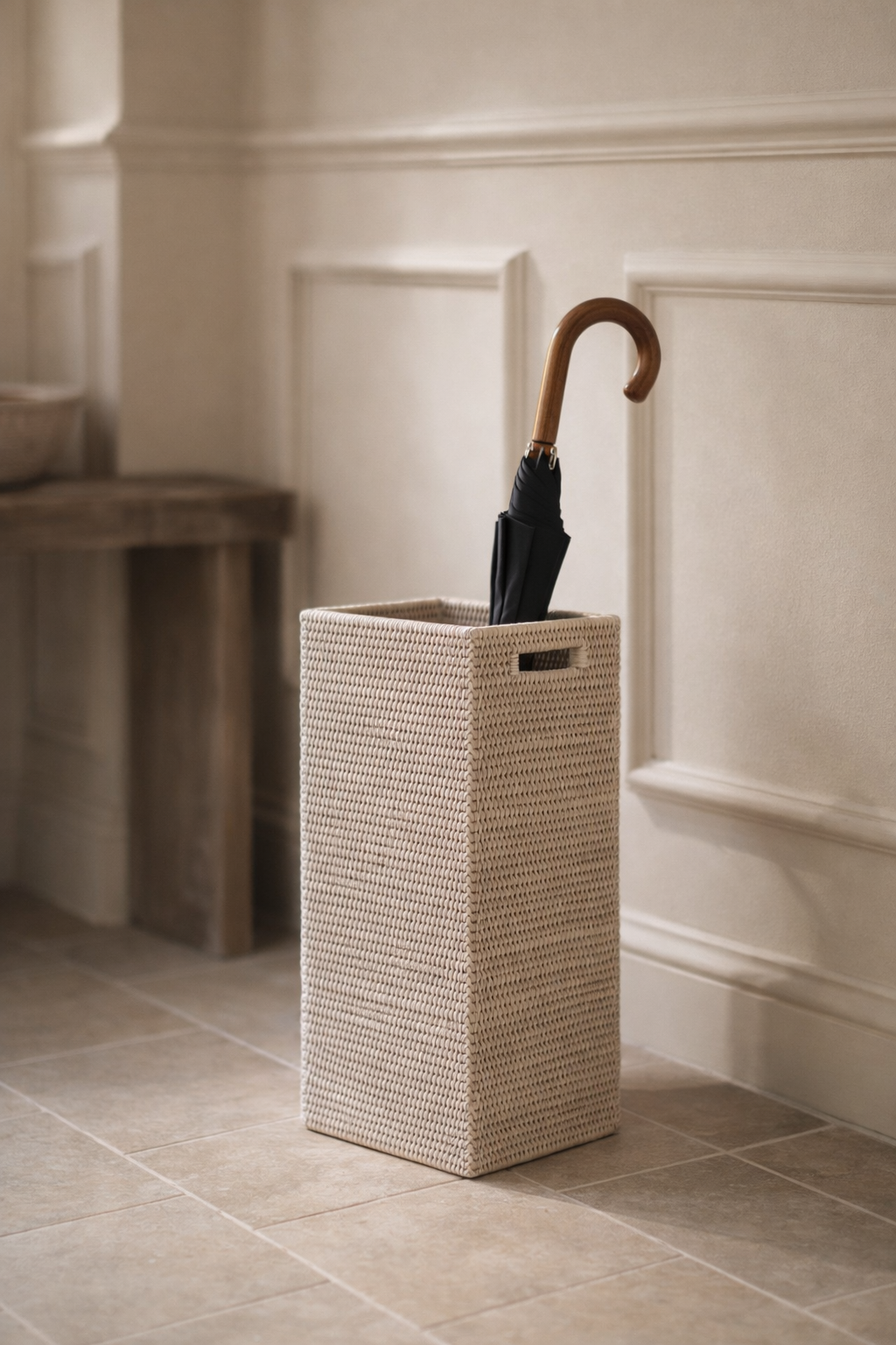 Wicker umbrella stand with an umbrella against a neutral wall.