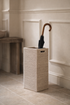 Wicker umbrella stand with an umbrella against a neutral wall.