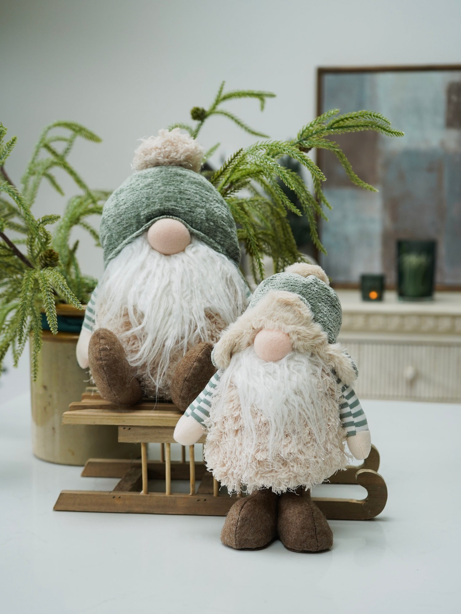 Two decorative gnomes gonks with green hats and brown boots in a home setting with plants and a fireplace.