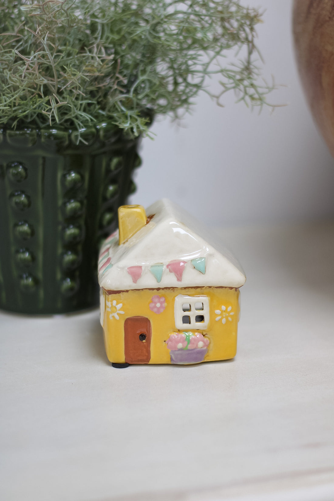 Small ceramic house with decorative elements on a white surface with a plant in the background