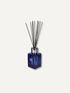 A reed diffuser with a faceted cobalt blue glass bottle, a silver metal collar, and several black reed sticks, shown against a plain off-white background.